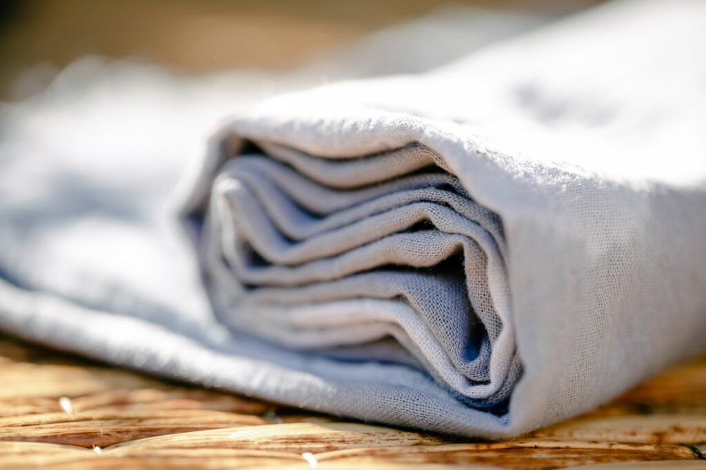 Closeup of rolled light linen natural textile placed on brown wicker surface on street with bright sunlight against blurred background